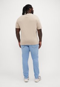 Beige kortermet t-skjorte kombinert med lyseblå jeans. T-skjorten har en rund halsutringning og en jevn tekstur. Skoene er grå med detaljer.