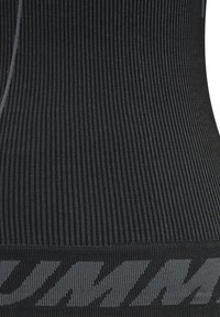 Svart stickad sporttopp med vertikal ribbdesign, med en grå logotyp vid basen, utformad för en figurnära silhuett. Slät textur.