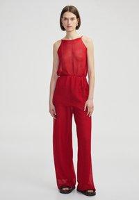 Conjunto rojo transparente de dos piezas que incluye una blusa sin mangas con lazo en la cintura y pantalones de pierna ancha, ambos con un patrón texturizado. Sandalias planas.