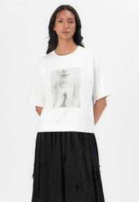 T-shirt bianco in cotone a maniche corte, con una stampa grafica centrale in bianco e nero di un volto e il testo "CPH MUSE".