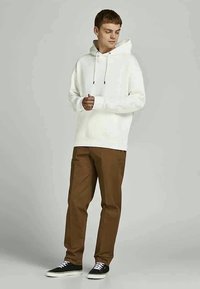 Sweatshirt branco com capuz e cordões, combinado com calças castanhas e ténis pretos com atacadores brancos. Design simples e casual.