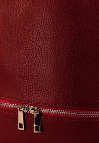 Gros plan sur du cuir rouge texturé avec une double fermeture éclair en argent partiellement fermée le long de la couture.