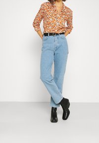 Koszula na guziki w kwiatowy wzór w kolorach pomarańczowym i białym, zestawiona z jasnoniebieskimi jeansami z wysokim stanem. Całość uzupełnia czarny pasek i botki za kostkę.