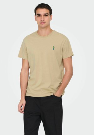 Beige katoenen t-shirt met korte mouwen, met een kleine groene cactus borduursel op de linkerkant van de borst. Gecombineerd met zwarte broek.