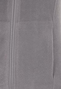 Graue Fleecejacke mit durchgehendem Reißverschluss, strukturiertem Material und Seitentaschen. Einfaches Design ohne sichtbare Muster oder Akzente.