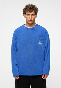 Blauw overhemd met lange mouwen, gemaakt van zachte stof, met een borstzak, voorzien van een gestructureerde uitstraling en geborduurd logo op de zak.