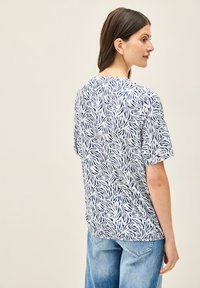 Top bianco a maniche corte con motivo foglia navy, vestibilità comoda e colletto a girocollo, abbinato a jeans in denim blu chiaro.