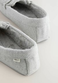 Pantofole grigie con un esterno in tessuto testurizzato, morbida fodera pelosa e una piccola etichetta "NEXT" sul lato. Forma a pantofola con suola piatta.