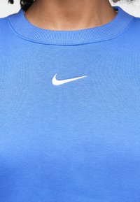 Φούτερ Nike σε υφάσμα με μπλε διαβάθμιση, με στρογγυλή λαιμόκοψη και ριμπ υφή, με λευκό λογότυπο στο κέντρο του στήθους.