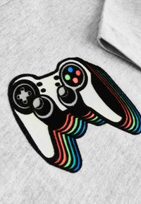 Graues Baumwoll-T-Shirt mit einem Grafikdesign eines Gamecontrollers, der farbenfrohe Knöpfe und regenbogenfarbene Streifen aufweist, die nach außen verlaufen.