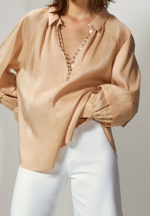 Jasnoróżowa lniana bluzka z dekoltem w serek, ozdobnymi guzikami z przodu i bufiastymi rękawami ze ściągaczami.