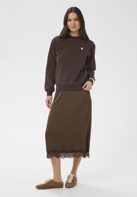 Rjava majica z dolgimi rokavi z rožnato obližem v obliki srca, kombinirana z rjavo midi krilo z čipkastim robom. Obleko dopolnjujejo rjavi semišasti čevlji.