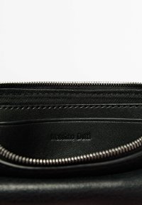 Interno di un portafoglio in pelle nera con chiusura a zip, caratterizzato da una texture liscia, un rivestimento in tessuto e il marchio "Massimo Dutti" in rilievo.