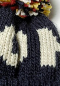 Gros plan sur un bonnet d'hiver bleu marine et blanc en tricot avec un pompon multicolore sur le dessus.
