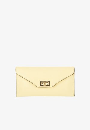 Prostokątny kremowy portfel typu kopertówka z klapką i złotym obrotowym zamkiem, gładka faktura skóry, bez widocznego paska.
