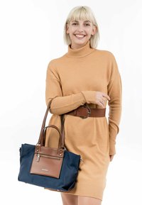 Borsa navy con dettagli in pelle marrone, forma rettangolare, tasca frontale con zip e manici robusti. Texture del tessuto liscia.