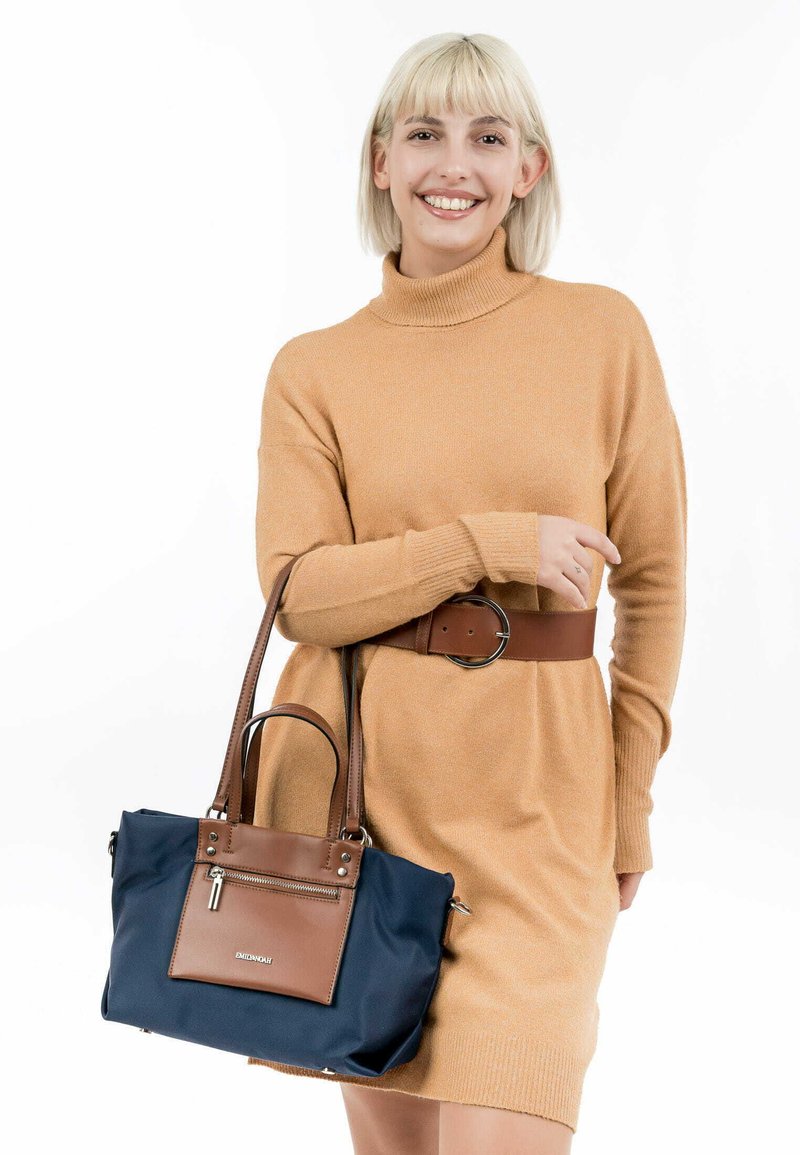 Borsa navy con dettagli in pelle marrone, forma rettangolare, tasca frontale con zip e manici robusti. Texture del tessuto liscia.