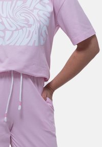 T-shirt rosa corto con un design grafico bianco, abbinato a pantaloni corti rosa con vita elastica e lacci.