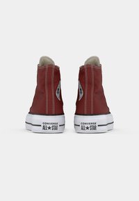 Punane kangast kõrge varreking, valgete kummitaldade ja mustade aktsentidega, millel on iga kandma Converse All Star logo.