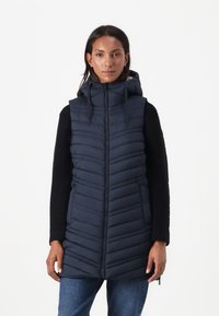 Marine blauwe puffer vest met verticale stiksels, ritssluiting aan de voorkant en een capuchon. Beschikt over een zwart gestructureerd breiwerk met lange mouwen aan de zijden.