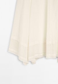 Abito beige chiaro con un orlo texturizzato e un corpetto liscio; presenta una silhouette fluida e un design a strati nella parte inferiore.
