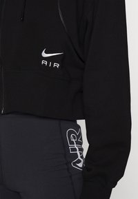 Svart cropped hoodie i fleece med dragkedja fram. Har en silverfärgad Nike-logga och texten "AIR" på bröstet, och texturen är slät.