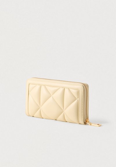 Portefeuille beige matelassé en cuir synthétique, doté d'une fermeture éclair et d'accentuations en métal doré. De forme rectangulaire avec une surface texturée.