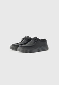 Black casual shoes with textured leather upper, rounded toe, and thick rubber sole featuring horizontal grooves and lace-up design.