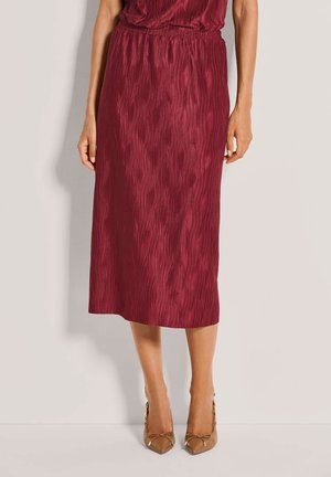 Bordeauxroter, plissierter Midirock mit strukturierten Wellenmustern, ausgestattet mit einem elastischen Bund, kombiniert mit transparenten, hellbraunen High Heels.