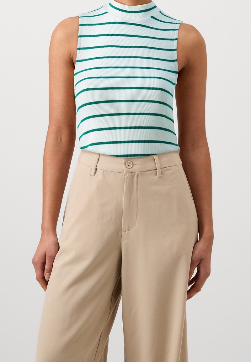 Haut blanc sans manches avec des rayures horizontales vertes, associé à un pantalon beige taille haute à jambes larges porté par une personne.