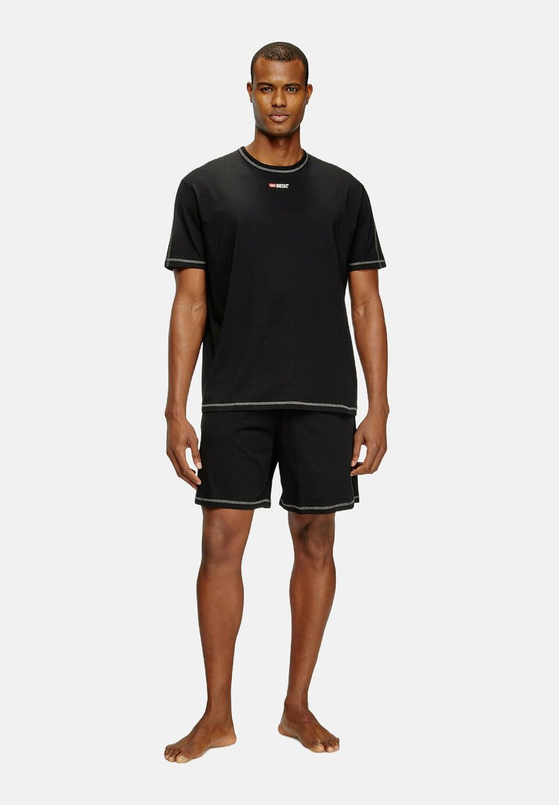 T-shirt noir à manches courtes et shorts assortis avec des coutures contrastées, présentant un petit logo sur la poitrine du t-shirt.