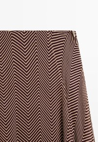 Gros plan sur un tissu à motif zigzag marron et beige avec une fermeture éclair latérale visible sur un vêtement.