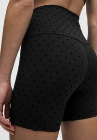 Kvinde iført højtaljede sorte cykelshorts med små prikker, som viser ryggen og den øverste del af låret.