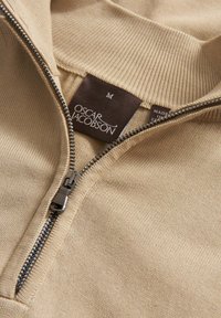 Maglione beige a zip con colletto alto, dotato di una zip argento e un'etichetta con "Oscar Jacobson" e taglia "M".