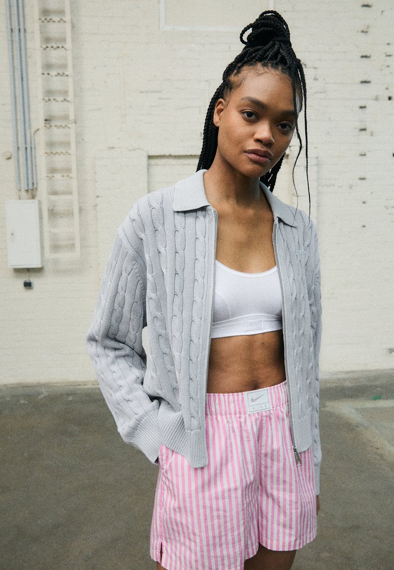 Gray cable-knit sweater with a collared neckline, paired with pink and white striped shorts featuring a logo patch.