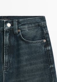 Mörka denimjeans har en hög midje-design med en snygg passform, synlig sömnad, metallknappdetaljer och klassiska fickor.