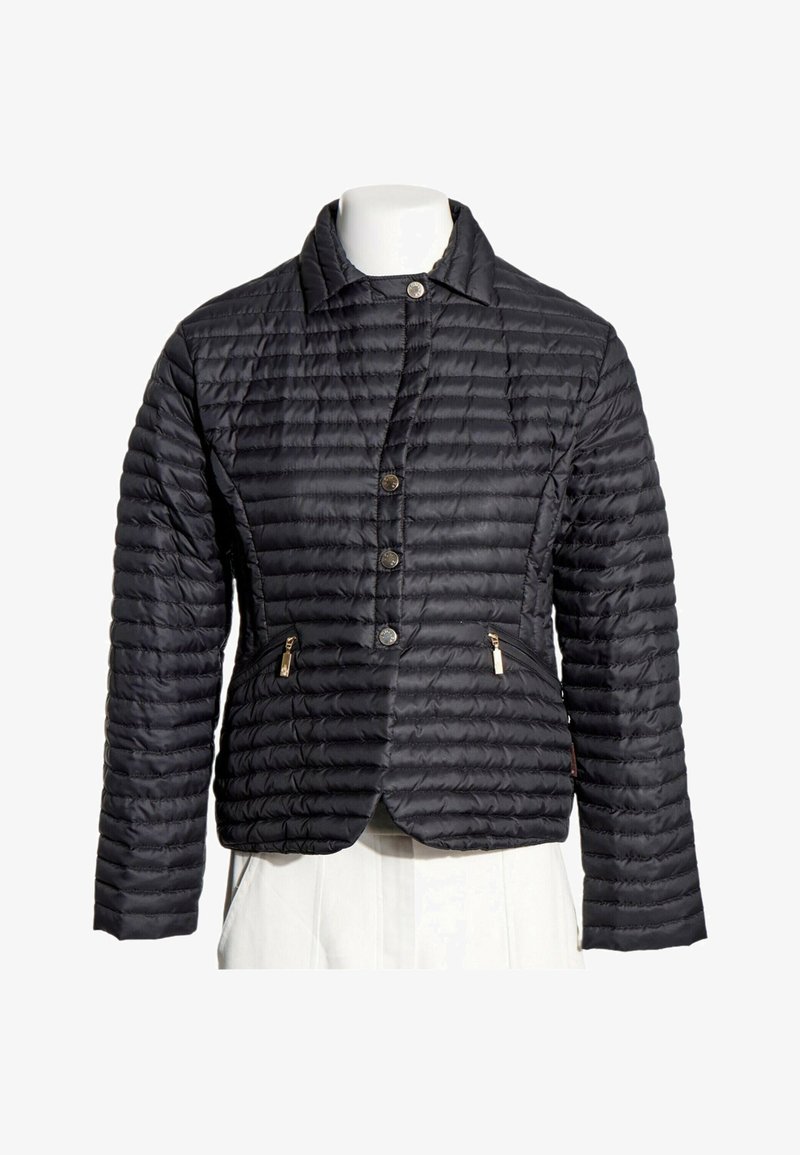 Veste légère matelassée noire avec manches longues, boutons sur le devant, col et deux poches zippées sur un torse de mannequin blanc.