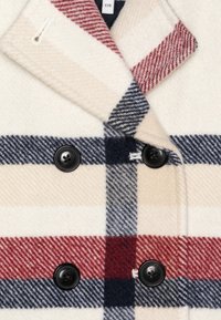 Abrigo de lana de doble botonadura en crema con un patrón de cuadros en rojo y azul marino, con botones negros y cuello con muesca. Textura suave.