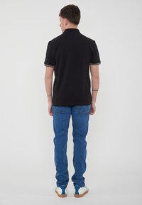 Polo shirt nero con colletto e maniche a contrasto, abbinato a jeans in denim blu e scarpe bianche con dettagli blu.