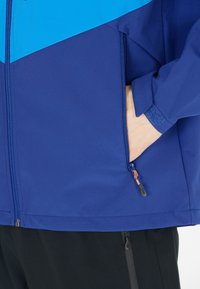 Blå och mörkblå jacka med framdragkedja, sidoficka och kardborreband på ärmsluten. Slät textur med kontrasterande färgsektioner.