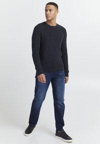 Marineblå striktrøje med rund halsudskæring, parret med blå jeans og sorte sneakers. Trøjen har et struktureret mønster.