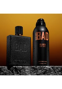 Bottiglia di profumo Black Diesel BAD nera e contenitore spray per il corpo nero abbinato con gocce d'acqua su una superficie in pietra strutturata su sfondo arancione.