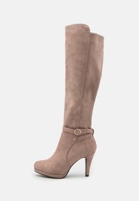 Botas de ante taupe hasta la rodilla con punta afilada y un tacón alto delgado, que presentan un cinturón decorativo con un acento de anillo dorado.