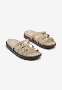Sandales beiges avec trois straps réglables et boucles métalliques. Semelle intérieure douce sur une semelle épaisse et sombre, présentant une texture lisse.