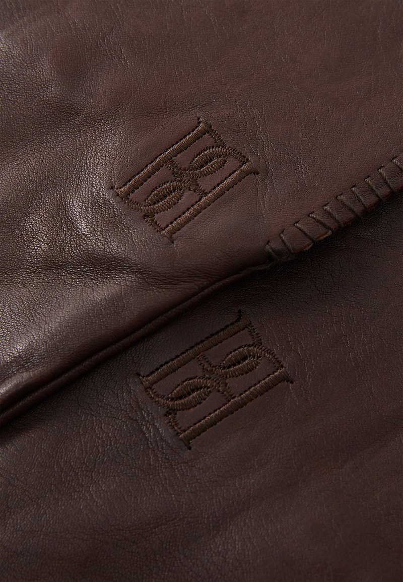 Brown leather gloves featuring embossed logo detail and contrasting stitching along the edge, showcasing rich texture and quality craftsmanship.