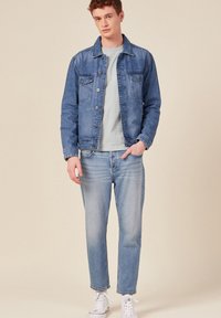 Farkkutakki keskisinisessä, jossa on rintataskut, suora leikkaus ja nappisuljenta. Yhdistetty vaaleansinisiin farkkuihin ja valkoisiin lenkkareihin.