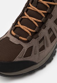 Chaussure de randonnée marron et grise avec tige en mesh, bout renforcé et lacets beige passés dans des œillets en tissu noir.