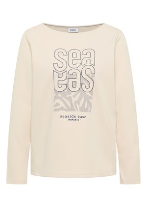 Chemise à manches longues crème avec le texte brodé "sea eas" et un motif de vagues, avec l'inscription "seaside ease moments" imprimée en dessous.