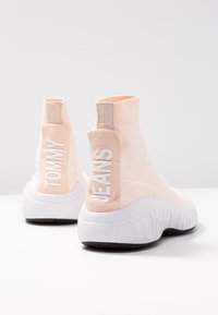 Roze gebreide enkelboots met witte rubberen zolen. Bevat een reliëf van het "TOMMY" en "JEANS" merk op de hiel. Gladde textuur, modern ontwerp.