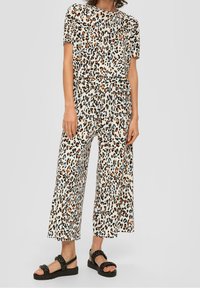 Tops w panterkowym wzorze i szerokie spodnie w kolorze kremowym z czarnymi, brązowymi i pomarańczowymi plamami; zestawione z czarnymi sandałami z plecionymi paskami.